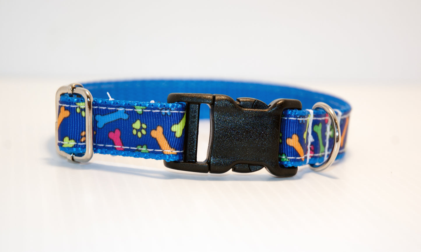 Multicolored pawprints and bones on blue background dog collar. 3/4" wide
